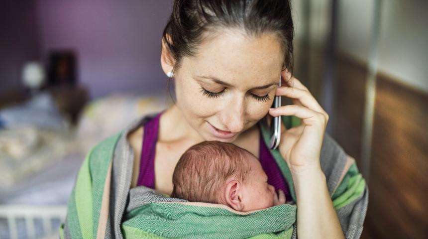 Mum holding baby in sling on phone