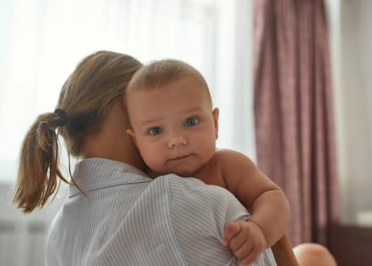 A baby looking over their mother's shoulder while being held.