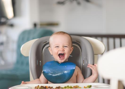 baby sitting in highchair laughing with food in front of them
