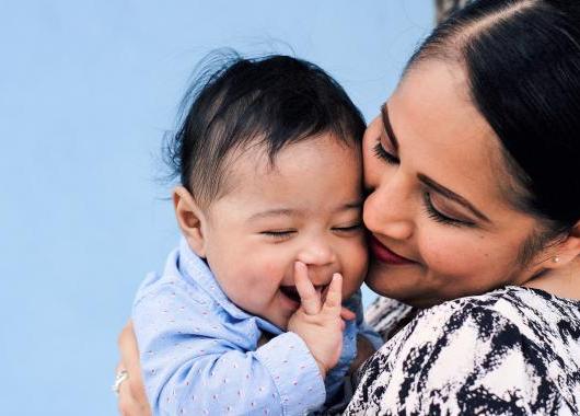 Mother smiling at her baby. baby has hands in its mouth.