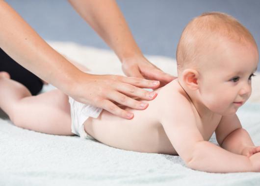 Baby lying on tummy with parent's hands massaging back.