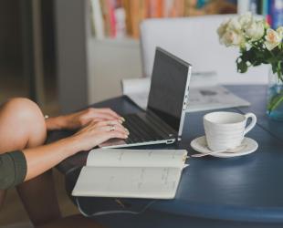 women sitting at a table with a tea cup working on a latptop