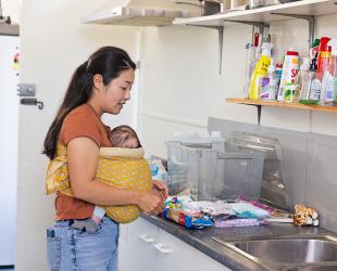 A mother with her baby in a sling looks for items in the kitchen of an evacuation centre.