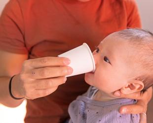 Woman cup feeds her baby using a disposal paper cup during an emergency