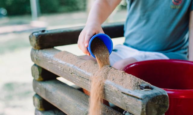 An image of a child pouring sand onto the wall of a sandpit