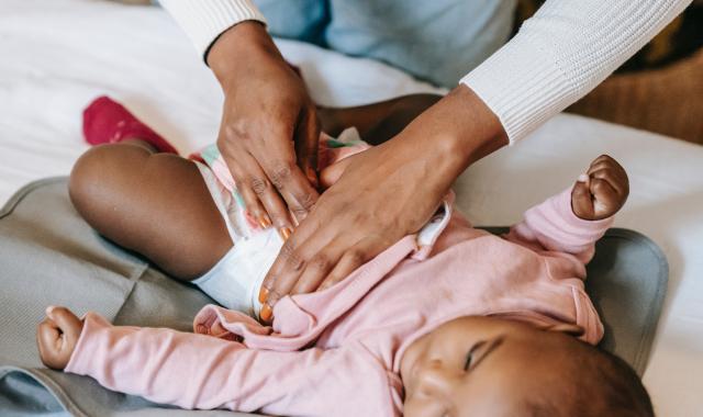 An image of a baby lying down. An adult is doing up its nappy after a change.