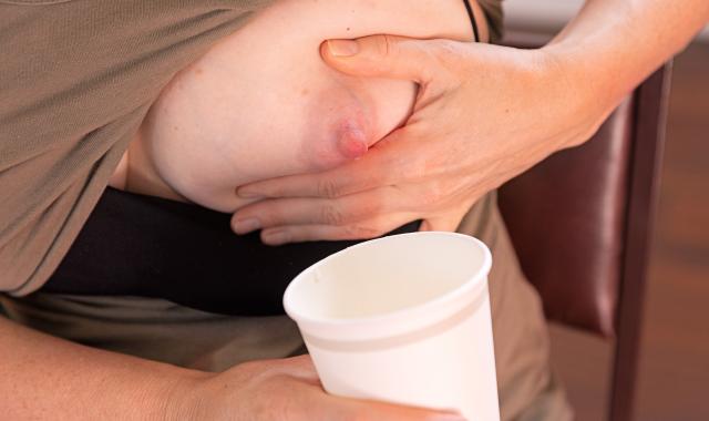 A woman hand expresses breastmilk into a paper cup during an emergency