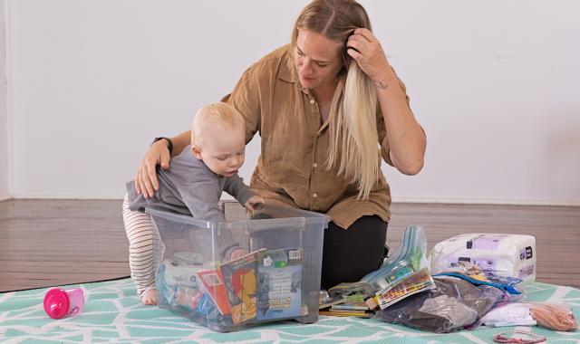 Woman with baby packing emergency supplies into a container.