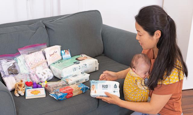 A woman with a young baby in a carrier sorts through emergency supplies