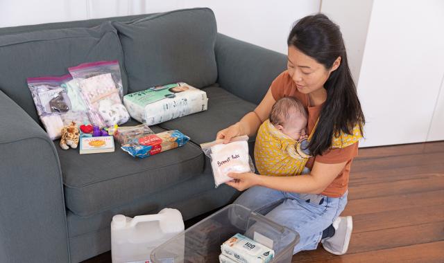 Woman with baby packing emergency supplies into a container.