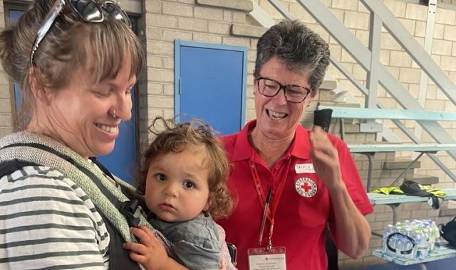 A mother with a baby in a carrier is supported by a volunteer in an evacuation centre.